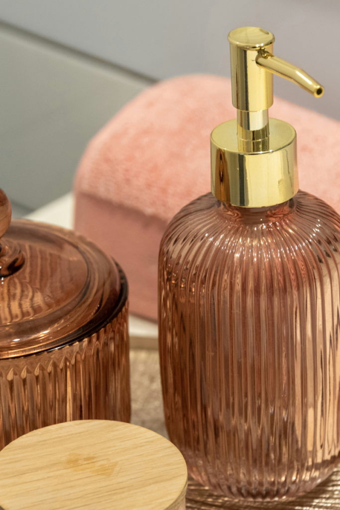 A ribbed amber glass soap dispenser with a gold pump and matching jar on a bathroom counter.