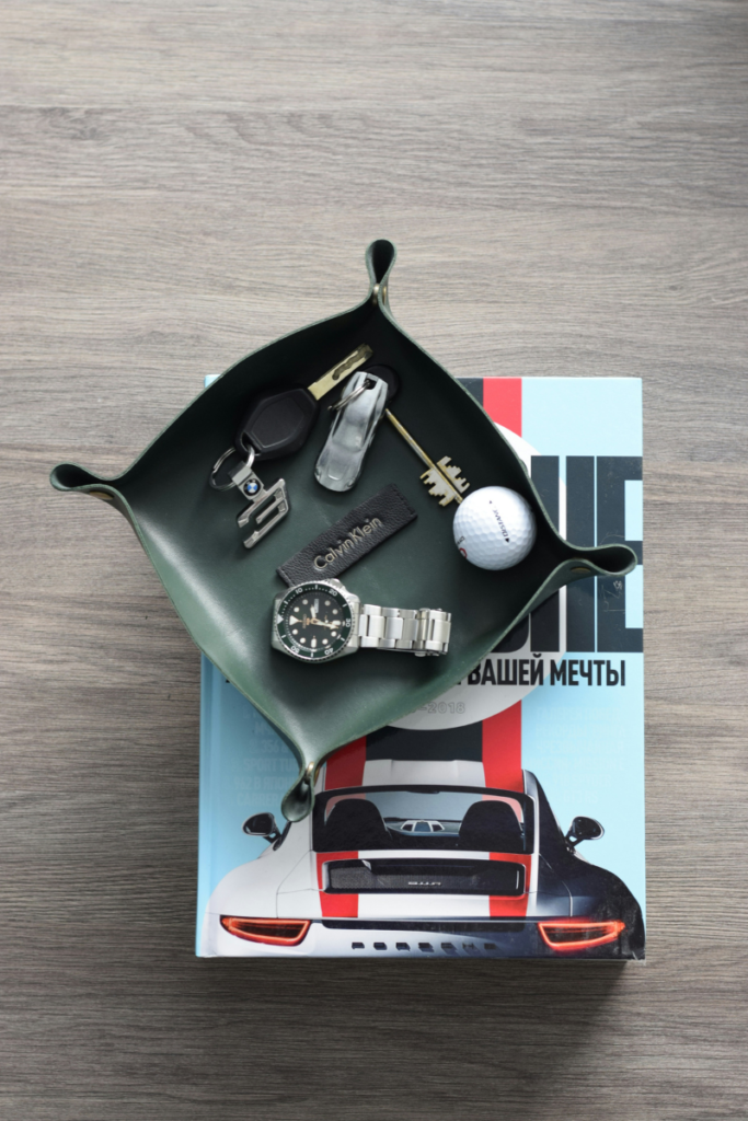 A forest green leather valet tray holding a watch and keys, placed on a coffee table book.