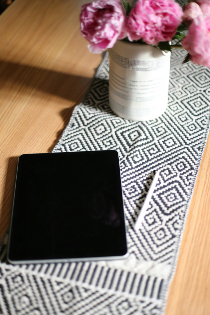 A black and white geometric pattern table runner on a wooden desk with a flower vase and tablet.